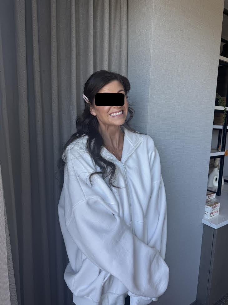 Lindsay P., smiling in a white zip-up sweatshirt with her hair styled for her wedding